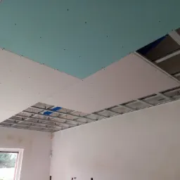 Montaż sufitu podwieszanego z płyty karton gips, widoczna metalowa konstrukcja i częściowo zamontowane płyty w kolorze białym i zielonym.