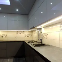 Nowoczesna kuchnia z ciemnymi, lakierowanymi frontami, jasnymi górnymi szafkami i blatem w odcieniach szarości, oświetlona punktowymi lampami sufitowymi i listwą LED pod szafkami, z płytkami...