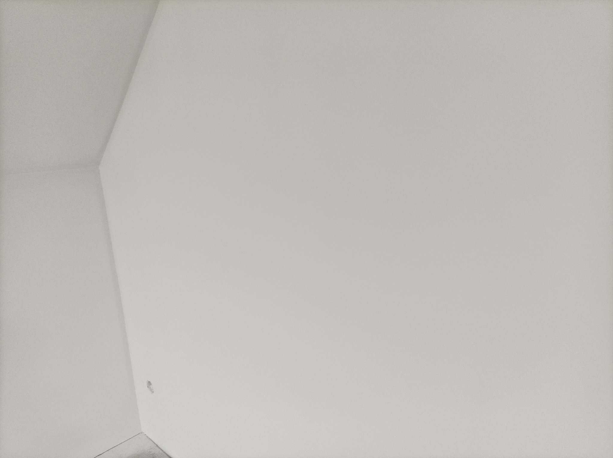 Świeżo pomalowany róg pomieszczenia z widocznym fragmentem podłogi i małym ubytkiem w ścianie. Ściana w jasnym, neutralnym odcieniu bieli.