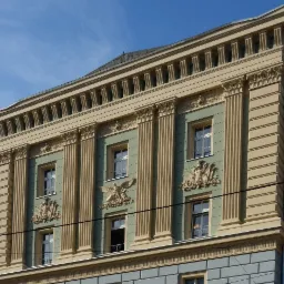 Elewacja budynku z kolumnami, dekoracyjnymi płaskorzeźbami, oknami i listwami w odcieniach beżu, zieleni i szarości pod błękitnym niebem.