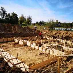 Wykonanie szalunku pod fundament domu jednorodzinnego w Kobysewie; widoczne zbrojenie wewnątrz formy, wykop, oraz pracownicy w tle.