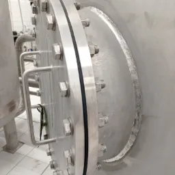 Szczegółowe ujęcie spawanej, okrągłej pokrywy zbiornika ze stali nierdzewnej, mocowanej na śruby, z widocznym spawem obwodowym i uchwytem transportowym.