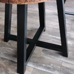 Stół z blatem z plastra drewna i czarnymi, metalowymi nogami o kwadratowym przekroju połączonymi poprzeczkami.