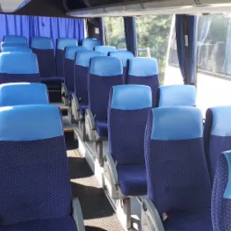 Wnętrze autobusu z rzędami niebiesko-granatowych foteli z zagłówkami, widok z przodu pojazdu.