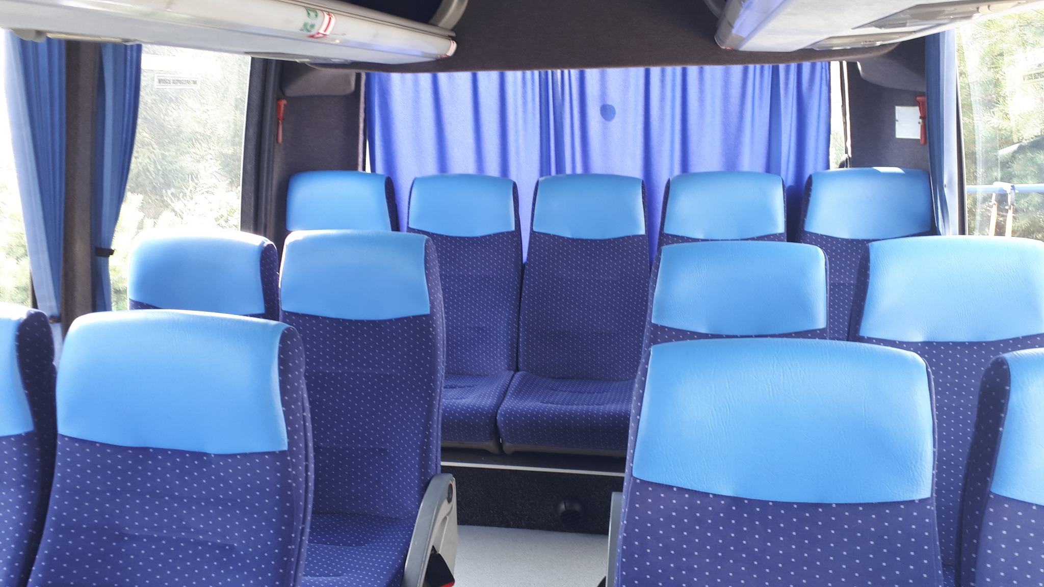 Wnętrze autobusu z niebieskimi siedzeniami i zasłonami, widok z przodu na puste fotele pasażerskie.