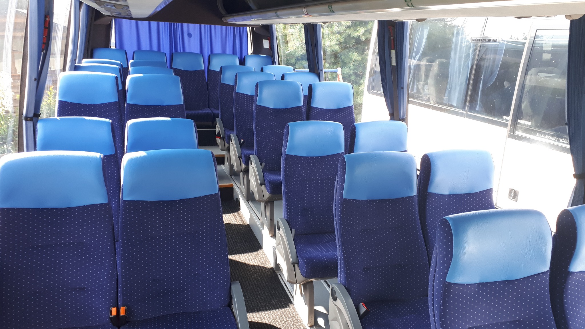 Wnętrze autobusu z rzędami niebiesko-granatowych foteli z zagłówkami, widok z przodu pojazdu.