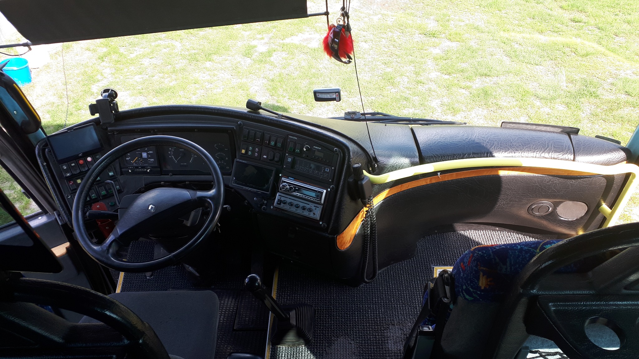 Kokpit autobusu Renault z widocznym radiem, panelem sterowania i kierownicą z logo Renault, widok z góry na zielone otoczenie.