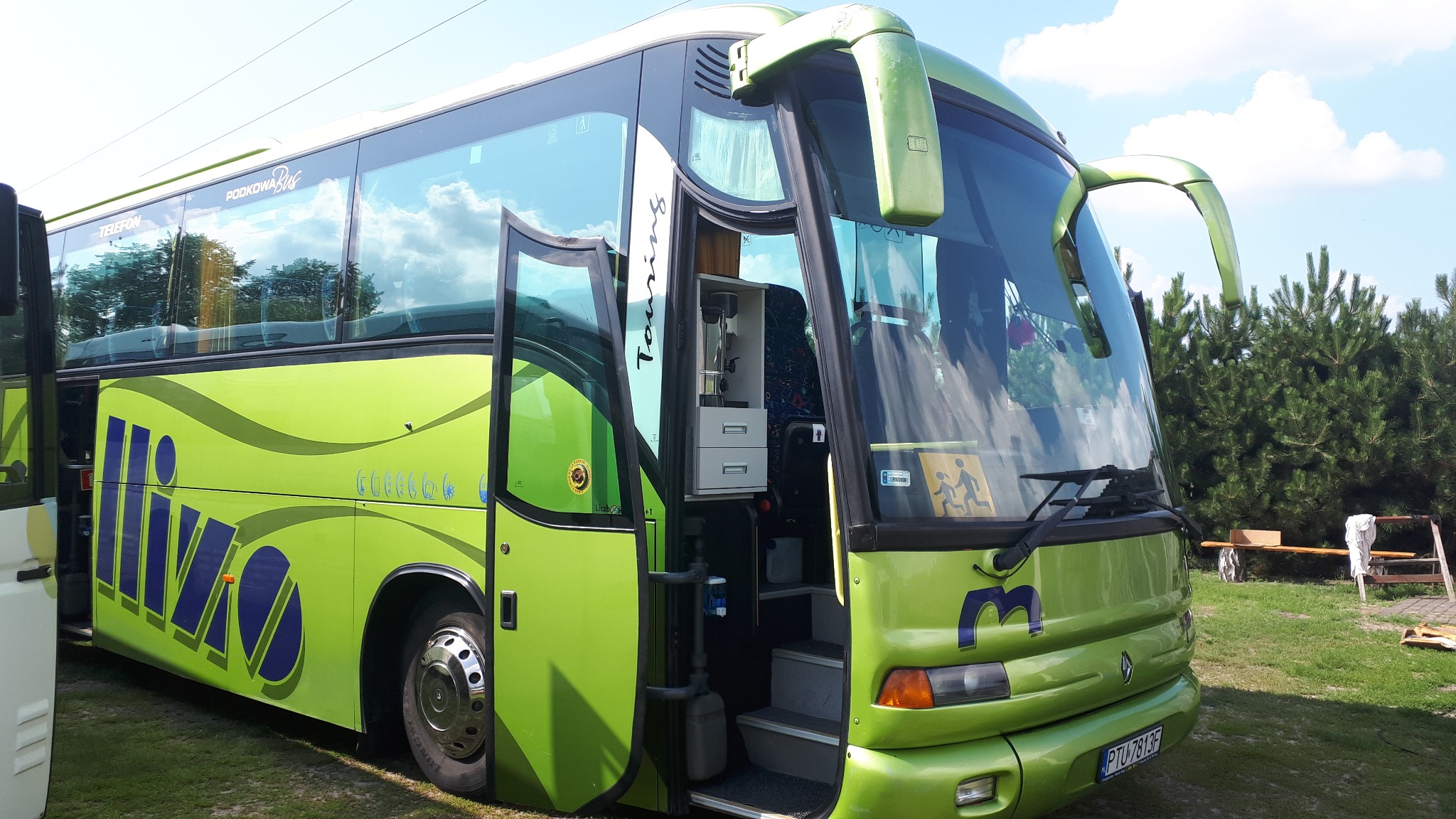 Zielony autokar turystyczny z otwartymi drzwiami wejściowymi, widoczne logo firmy przewozowej oraz tabliczka informacyjna o przewozie dzieci.