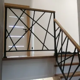 Nowoczesna balustrada schodowa z czarnych, przecinających się metalowych prętów i drewnianych poręczy, widok z dołu, oświetlenie dzienne.