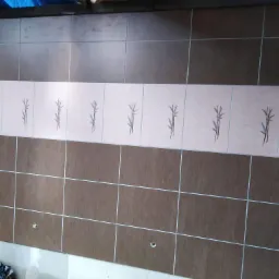 Ułożone brązowe i beżowe płytki ścienne z motywem roślinnym, widoczne otwory na armaturę, fragment worka na gruz przy podłodze.