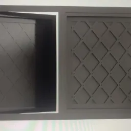 Metalowa szafka z otwartymi drzwiczkami, z dekoracyjnym wzorem rombów na froncie, pomalowana na szaro.