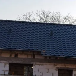 Nowy dach z ciemnej dachówki ceramicznej na surowym budynku z pustaków, widoczne kominki wentylacyjne.
