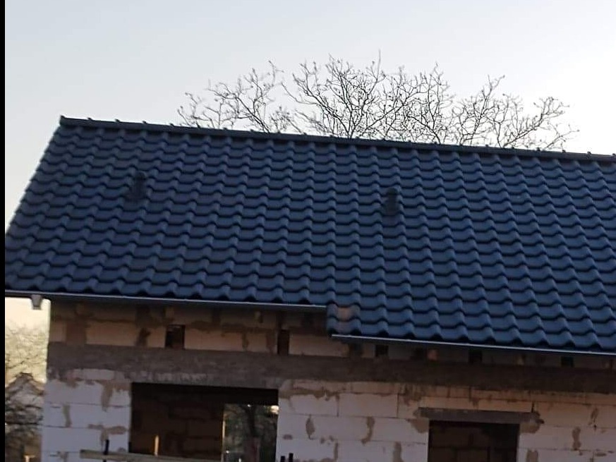 Nowy dach z ciemnej dachówki ceramicznej na surowym budynku z pustaków, widoczne kominki wentylacyjne.