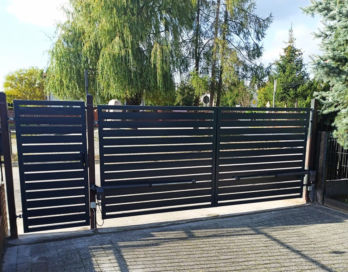 Nowoczesna, pozioma brama wjazdowa w kolorze antracytowym z automatyką, widziana z zewnątrz posesji, z zielonym drzewem w tle.