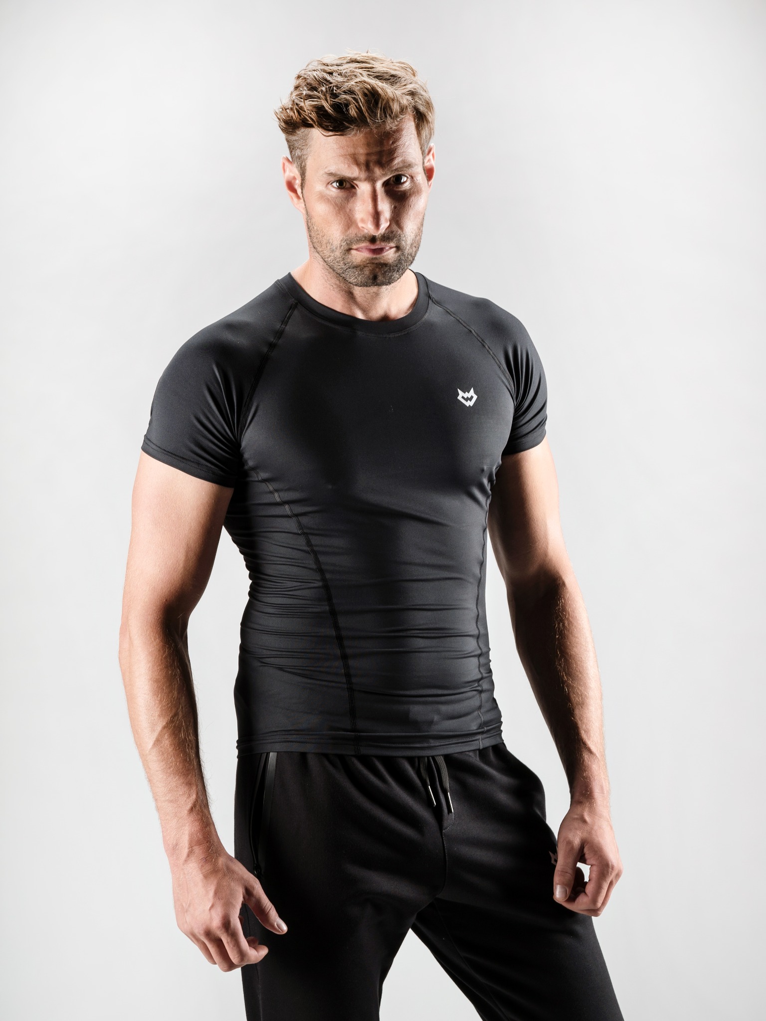 Mężczyzna w czarnej, dopasowanej koszulce sportowej z logo WHITEWOLF na tle studyjnym, pozujący do zdjęcia produktowego.