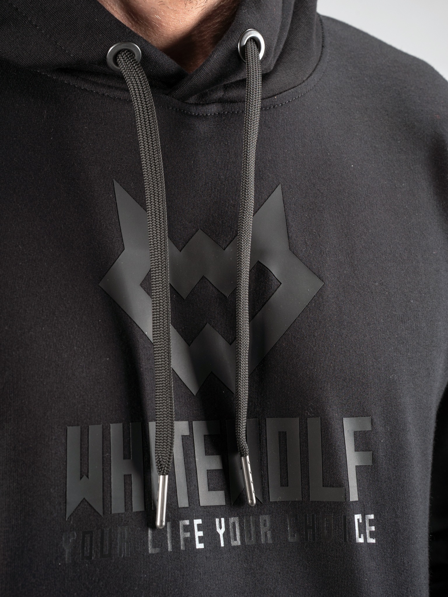 Czarna bluza z kapturem marki White Wolf z czarnym logo i napisem 'YOUR LIFE YOUR CHOICE' na klatce piersiowej, widoczne sznurki z metalowymi końcówkami.