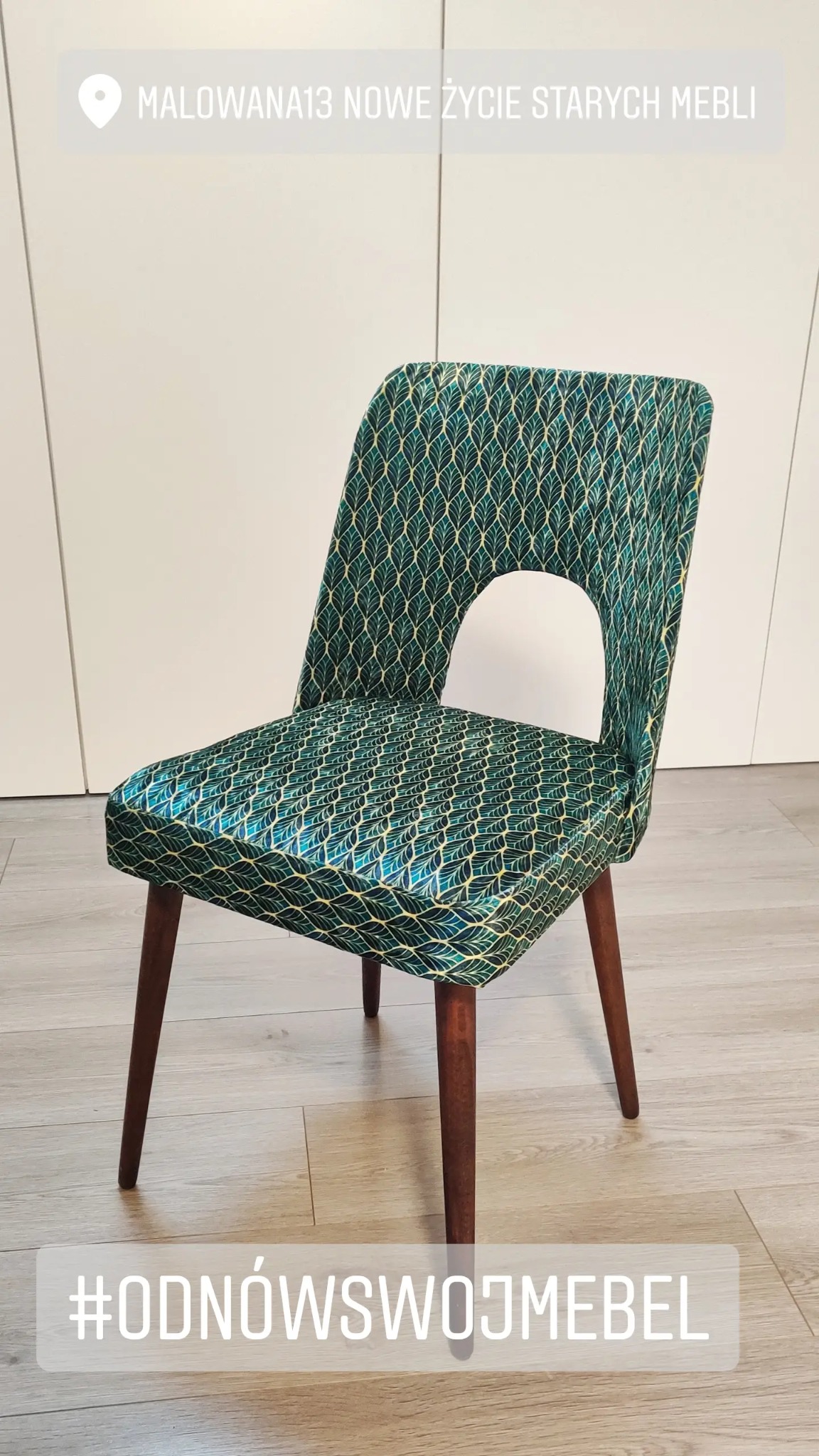 Krzesło po renowacji tapicerskiej, obite zieloną tkaniną w złote liście, z okrągłym wycięciem w oparciu, na tle białej szafy i jasnej podłogi.