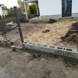 Usługi remontowo budowlane - Wznoszenie fundamentu z betonowych bloczków na posesji, widoczne pręty zbrojeniowe i taśma ostrzegawcza.