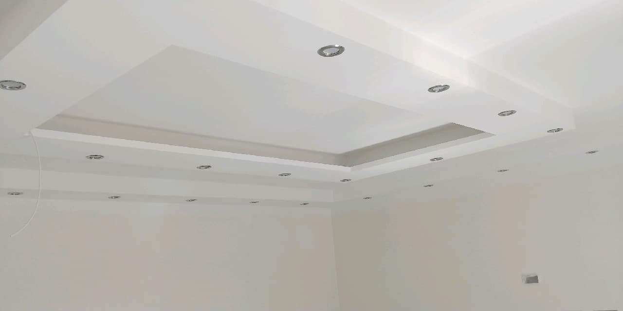 Biały sufit podwieszany z wbudowanymi punktowymi lampami LED, tworzący kwadratowy wzór z obniżonym środkiem, świeżo pomalowane ściany w tle.