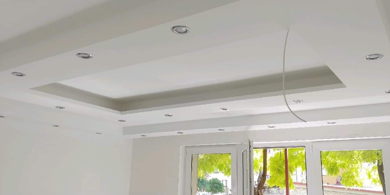 Biały sufit podwieszany z oświetleniem punktowym w nowocześnie wykończonym wnętrzu, widoczna instalacja elektryczna przed montażem opraw.