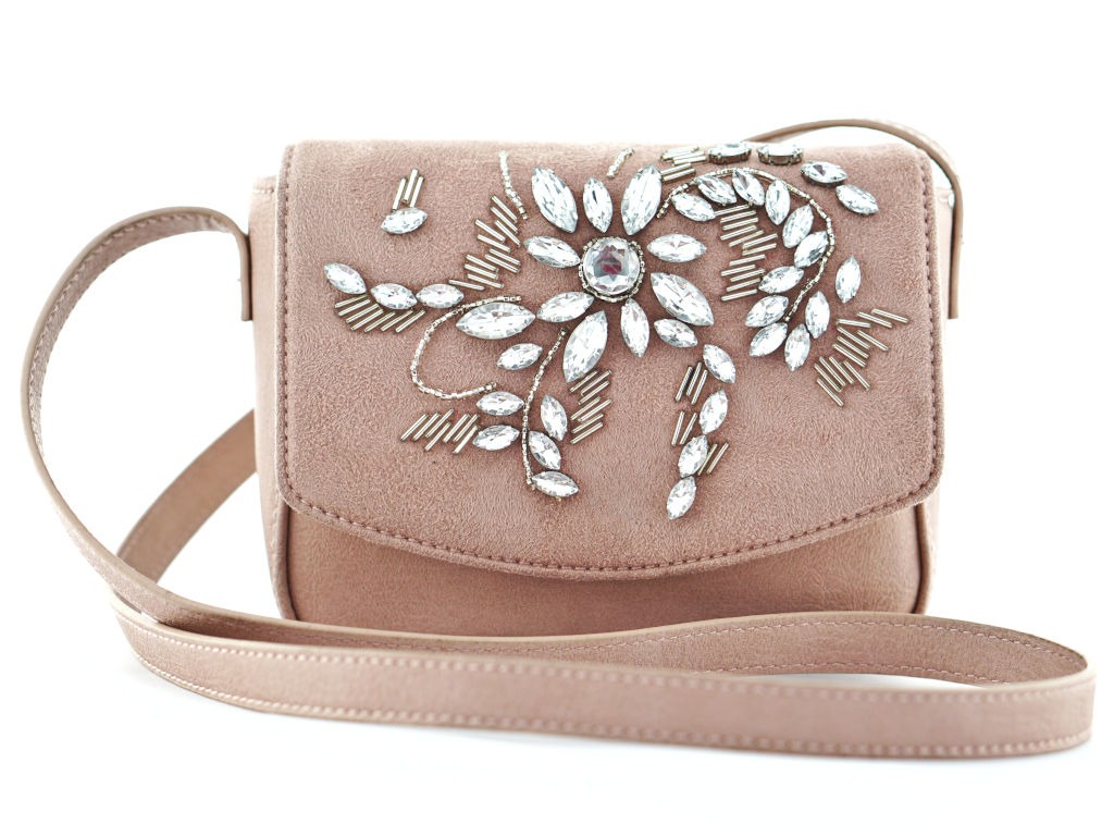 Mała, pudrowo-różowa torebka z klapką, zdobiona aplikacją w kształcie kwiatu z błyszczących kryształków i srebrnych koralików, na białym tle.