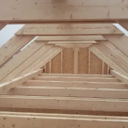 Konstrukcja drewniana dachu w trakcie budowy, widoczne elementy więźby dachowej i poszycie z płyty OSB, w tle zabudowa mieszkalna w pochmurny dzień.