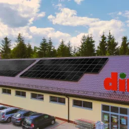 Instalacja fotowoltaiczna na dachu sklepu Dino w Rzeszowie, widok z parkingu z zaparkowanymi samochodami i firmowym vanem w tle.