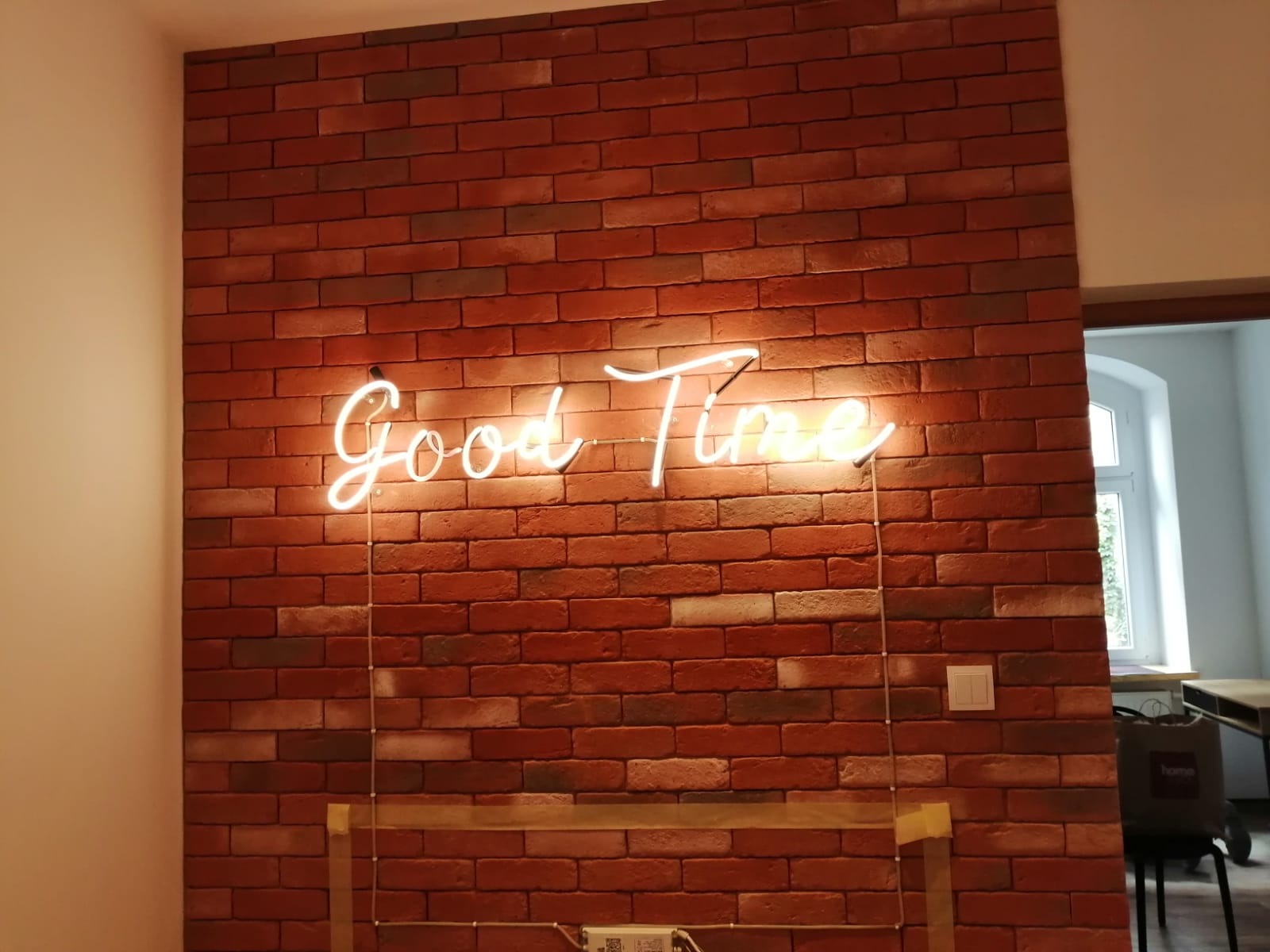 Ściana z cegły klinkierowej z neonowym napisem 'Good Time', oświetlenie boczne podkreśla fakturę cegieł.