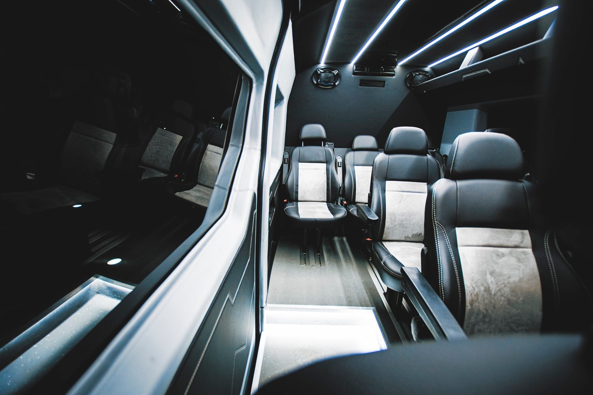 Wnętrze luksusowego busa z czarną tapicerką, podświetlanym sufitem i skórzanymi fotelami z jasnymi wstawkami, widok z przodu kabiny pasażerskiej.