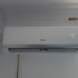 KrisCold - Biała klimatyzacja marki Gree zamontowana na ścianie, ustawiona na 22 stopnie, widoczna część okna i karnisza.