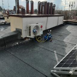 KrisCold - Zewnętrzna jednostka klimatyzatora LG zamontowana na dachu budynku, podłączona do pompy próżniowej, obok panel słoneczny, widoczne przewody i narzędzia.