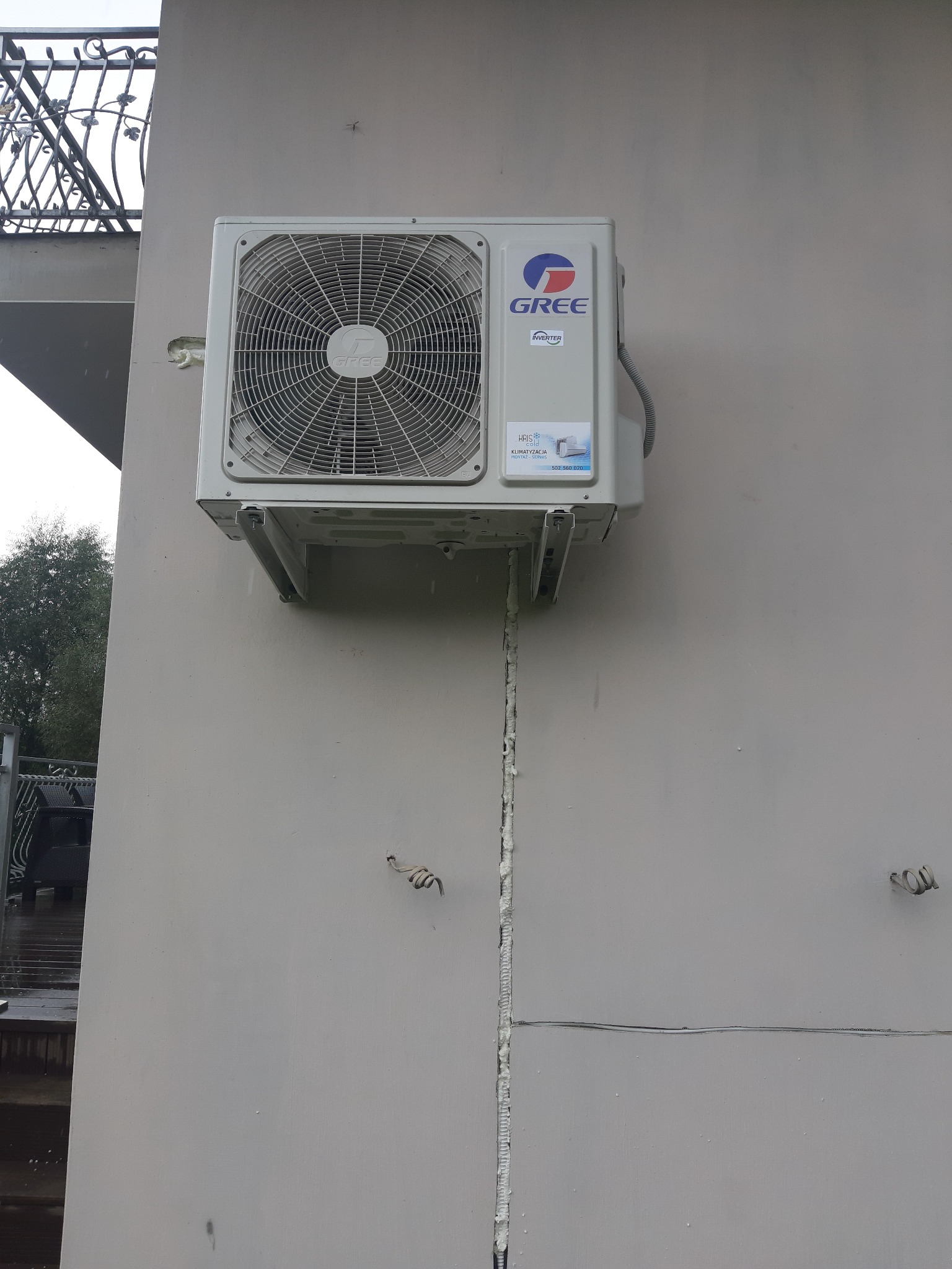 Zewnętrzna jednostka klimatyzacji marki Gree zamontowana na elewacji budynku z widocznymi przewodami zabezpieczonymi pianką montażową.