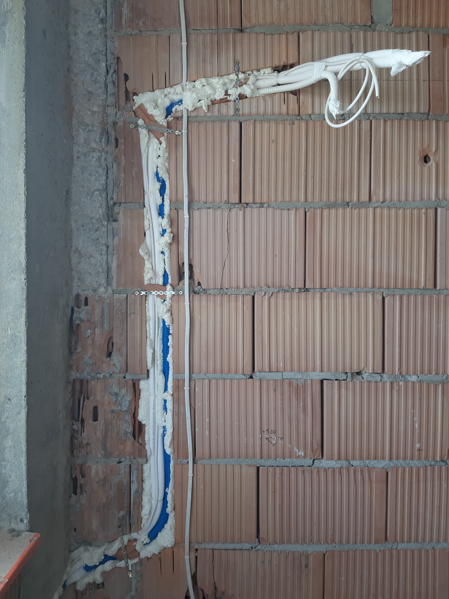 Montaż przewodów klimatyzacji w bruzdach ściany z cegły, zabezpieczonych pianką montażową i przymocowanych metalowymi uchwytami.