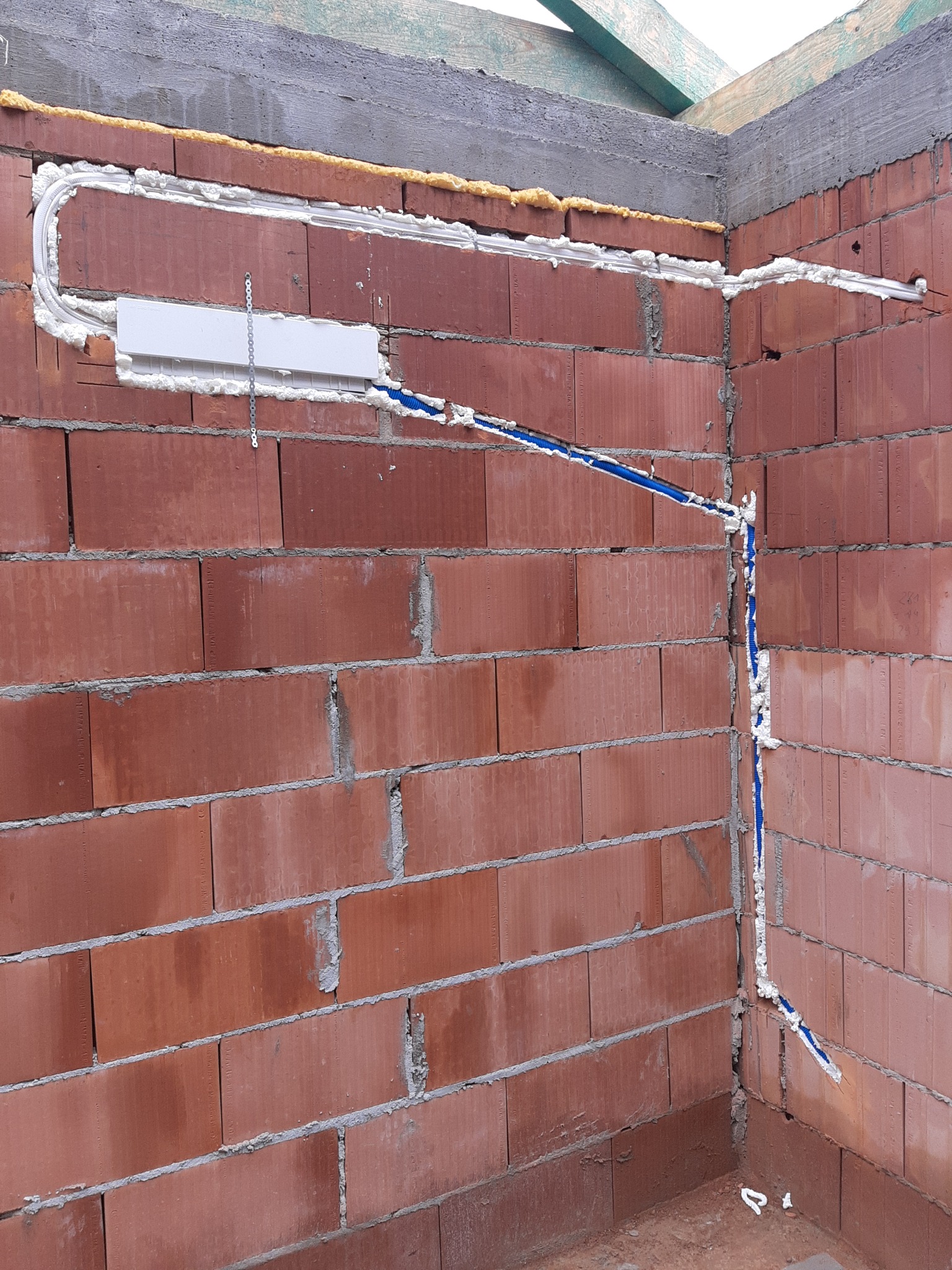 Montaż instalacji chłodniczej w nowym budynku: widoczne rury w izolacji piankowej prowadzone wzdłuż ceglanej ściany, z zamontowaną skrzynką przyłączeniową i metalową listwą montażową.