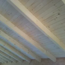 Konstrukcja drewniana dachu z widocznymi belkami nośnymi i deskowaniem, surowe drewno, widok od wewnątrz.