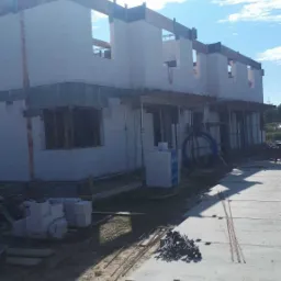 Wznoszenie ścian z bloczków białych na budowie szeregówki, widoczne zbrojenia i materiały budowlane Silka oraz elementy szalunkowe.