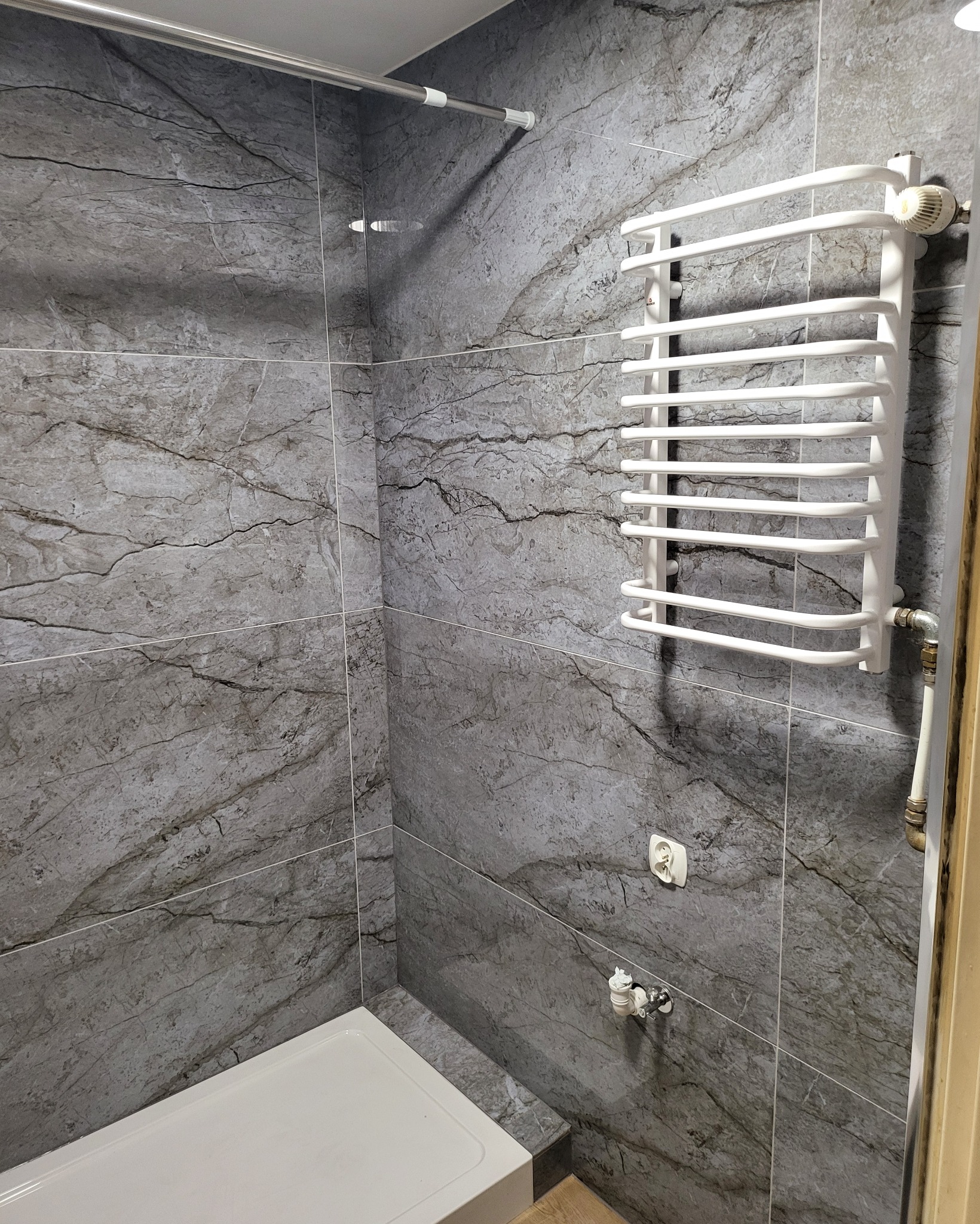 Szara łazienka z płytkami imitującymi marmur, biały grzejnik drabinkowy, brodzik i chromowana armatura.