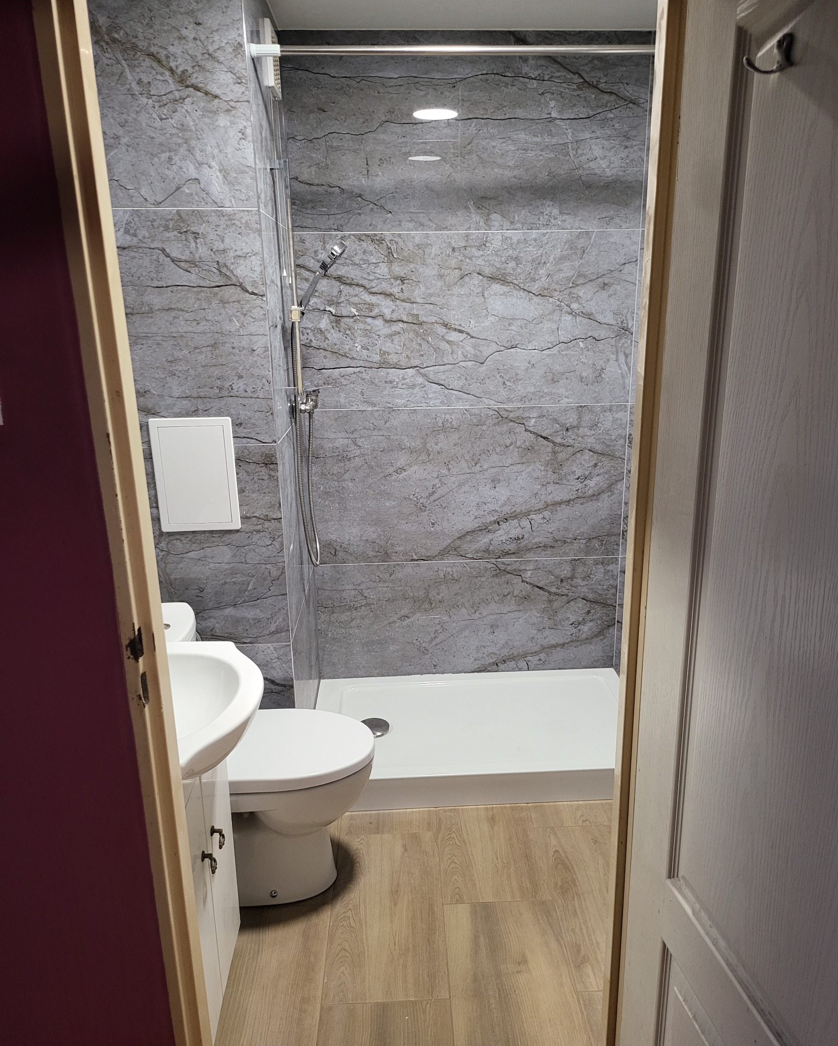 Wykończona łazienka w Gniewkowie z szarymi płytkami imitującymi marmur, kabiną prysznicową z brodzikiem, umywalką z szafką i toaletą, widok przez otwarte drzwi.