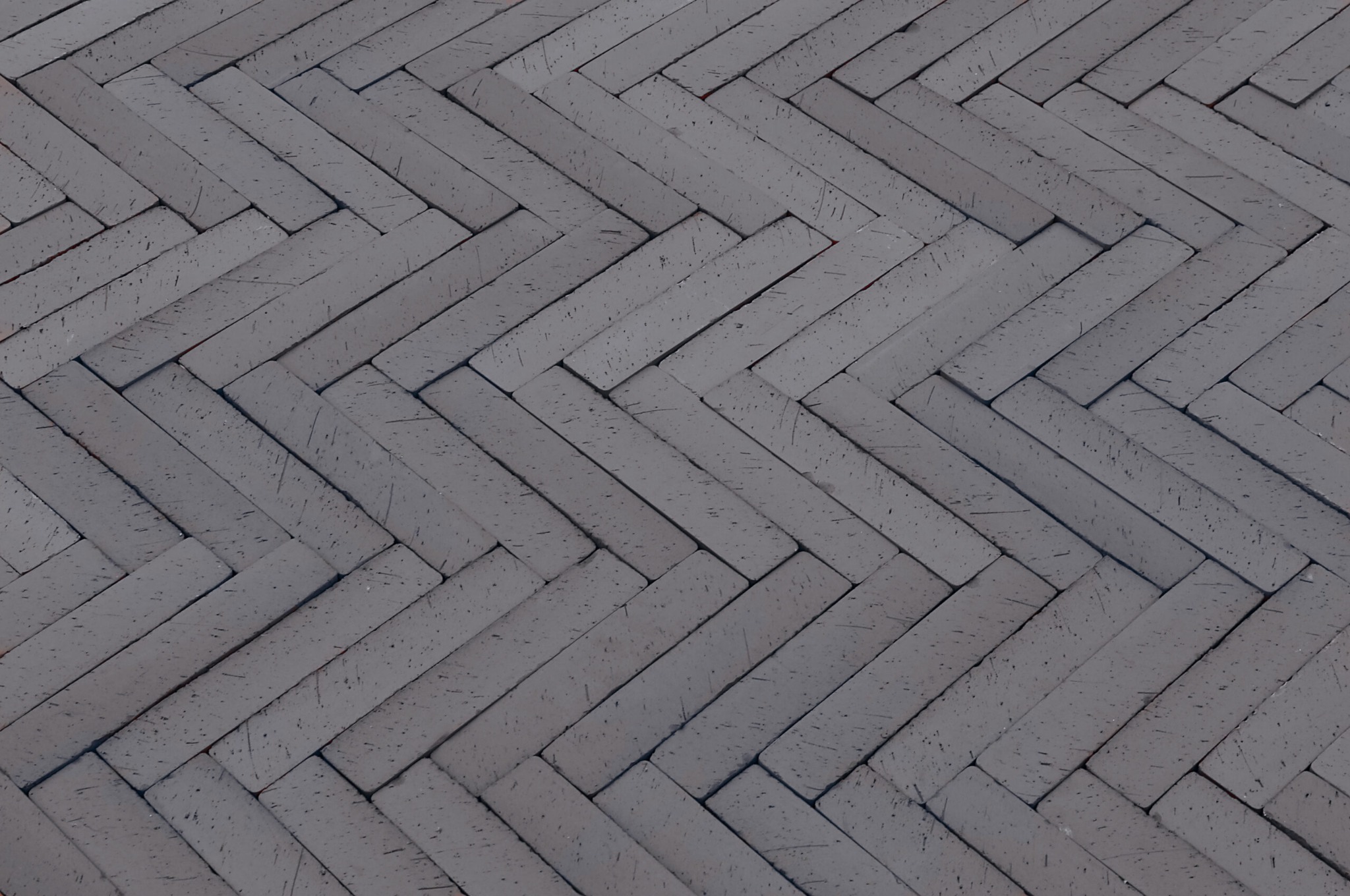 Ułożona w jodełkę szara kostka brukowa, widok z góry, widoczne drobne rysy na powierzchni kostki.