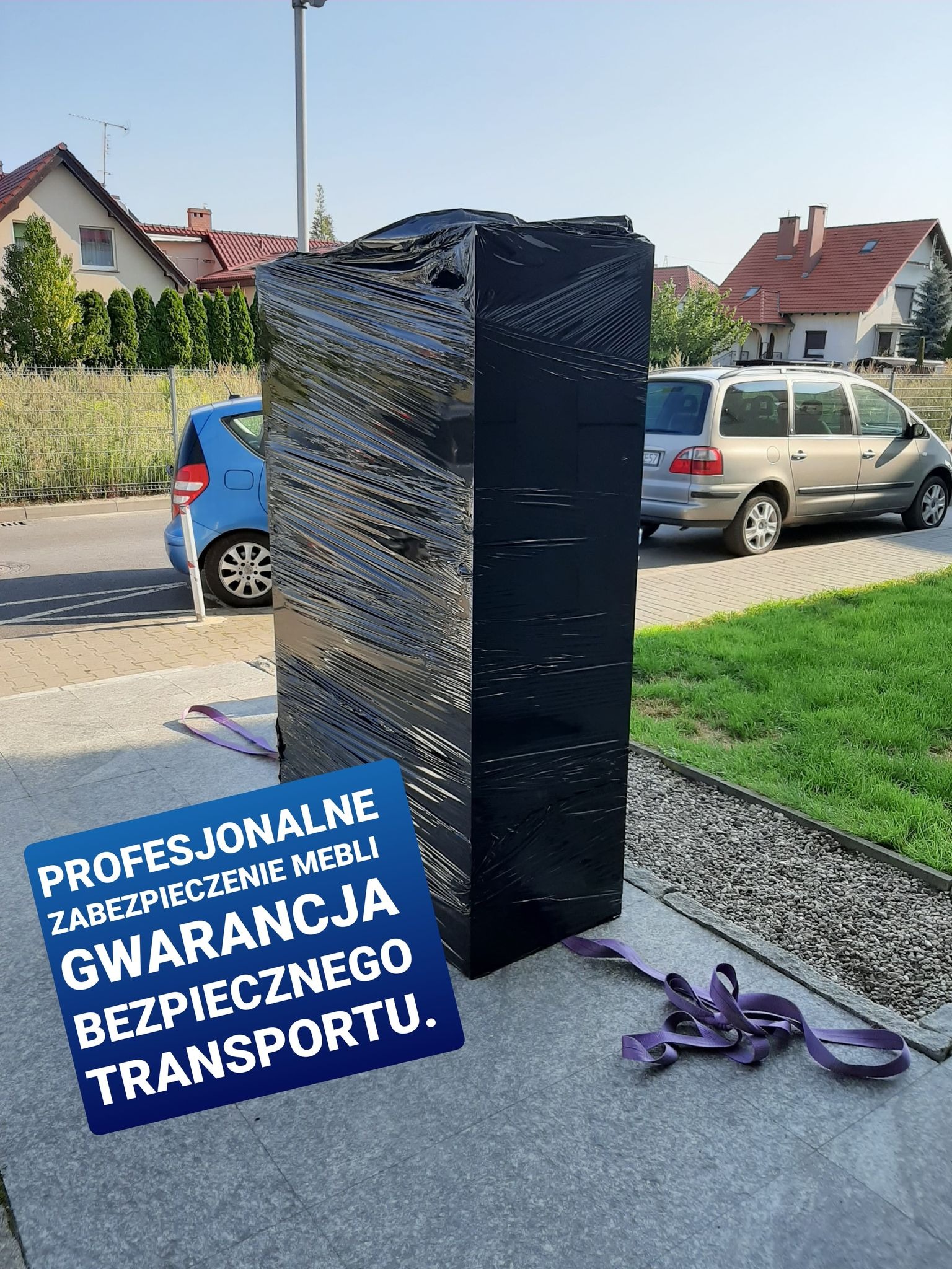 Mebel owinięty folią stretch, zabezpieczony pasami transportowymi, gotowy do transportu na chodniku przed domem.
