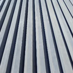 Szare prefabrykaty betonowe ułożone równolegle, tworzące wzór z cieniem, widoczne z perspektywy.