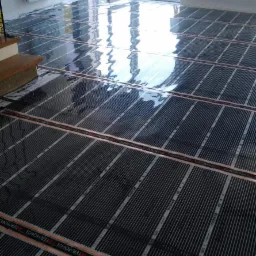 Maty grzewcze pod podłogą, system ogrzewania podłogowego marki TERMOFOL w jasnym pomieszczeniu z dużymi oknami tarasowymi.