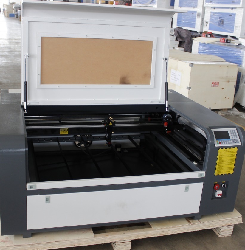 Otwarta obudowa maszyny do cięcia laserowego z widocznymi prowadnicami i panelem sterowania, umieszczona na drewnianej palecie.