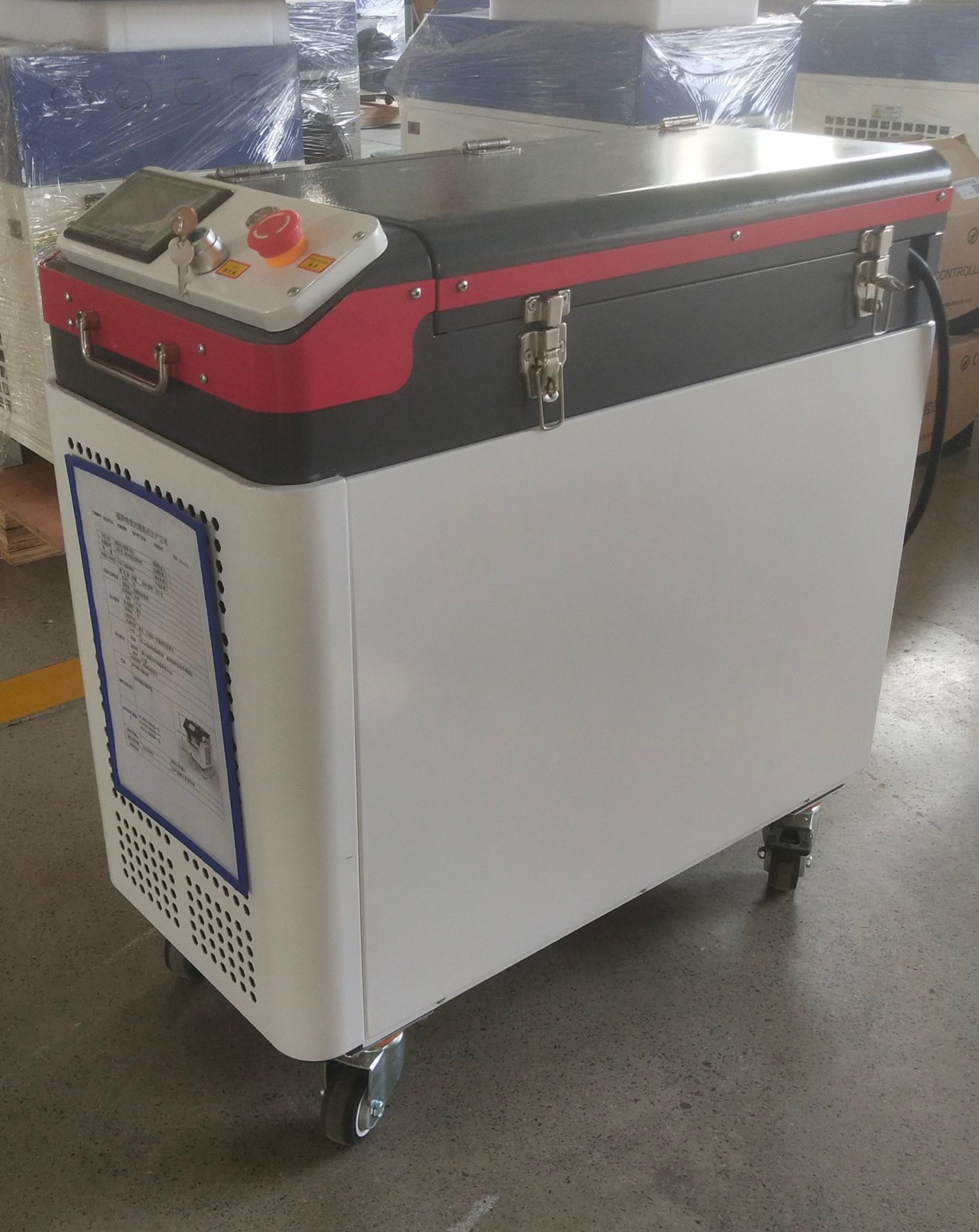 Przenośne urządzenie do obróbki metali laserem z panelem sterowania, kluczykiem w stacyjce i przyciskiem bezpieczeństwa, na kółkach, z dokumentacją techniczną na boku.