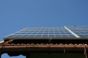 Panele słoneczne na dachu z brązowej dachówki, zamontowane w Nowym Sączu, widoczne na tle błękitnego nieba.