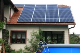 Panele fotowoltaiczne na dachu domu jednorodzinnego z czerwonej dachówki, widoczne okno, fragment basenu i drabinka.