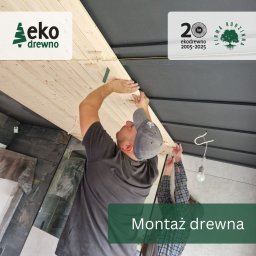 EKODREWNO - Montaż drewnianej boazerii sufitowej przez dwóch monterów. Widoczne logo firmy Eko Drewno i elementy konstrukcyjne sufitu. Ujęcie z dołu, podkreślające etap prac.