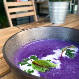 Illegal Taste Catering - Fioletowa zupa krem w ciemnej misce, udekorowana kleksami śmietany i świeżymi ziołami na drewnianym stole w restauracji.