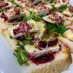 Illegal Taste Catering - Apetyczne kanapeczki z białym serem, konfiturą z czerwonych owoców i świeżymi kiełkami, ułożone na białej tacy cateringowej.