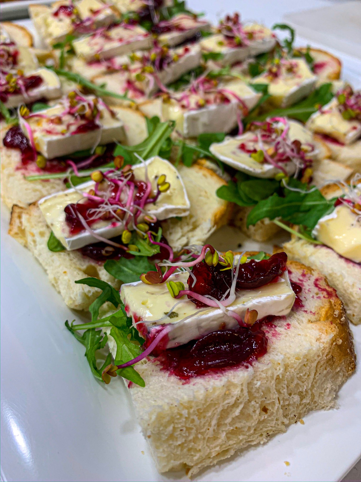 Apetyczne kanapeczki z białym serem, konfiturą z czerwonych owoców i świeżymi kiełkami, ułożone na białej tacy cateringowej.